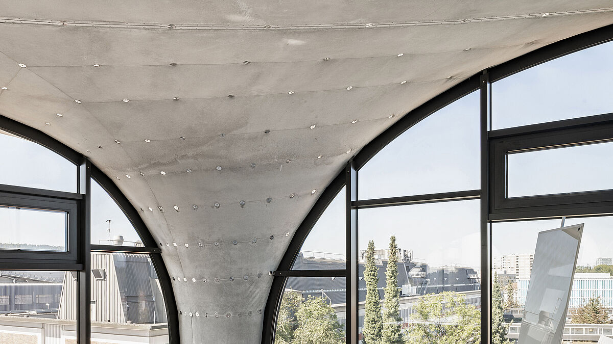 Les éventuels affaissements et mouvements de la légère voûte en béton sont neutralisés par des mécanismes ajustables dans les profilés de fixation de la façade en poteaux-traverses.